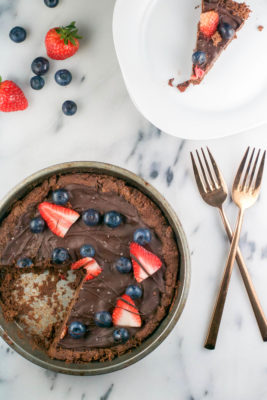 You haven't lived until you've tried this Flourless Chocolate Cookie Pizza recipe. A chocolate peanut butter cookie is smeared with dark chocolate and topped with fresh blueberries, strawberries, and sea salt for a delicious take on a gluten-free cookie pizza.