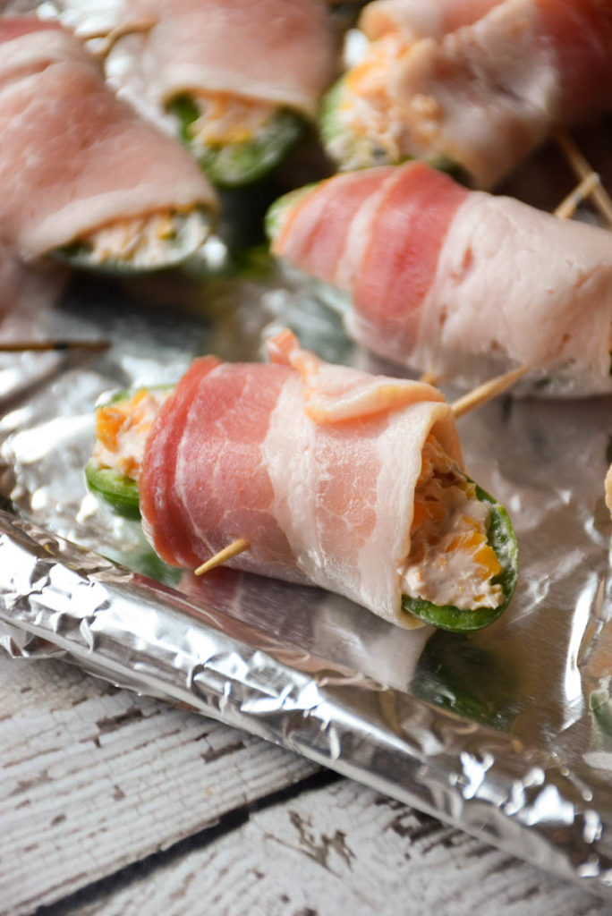 Sweet Bacon Wrapped Jalapeño Poppers are filled with cream cheese and cheddar cheese that has been blended with raspberry jam then wrapped in a blanket of salty bacon! This sweet heat treat will make crowds beg for more!