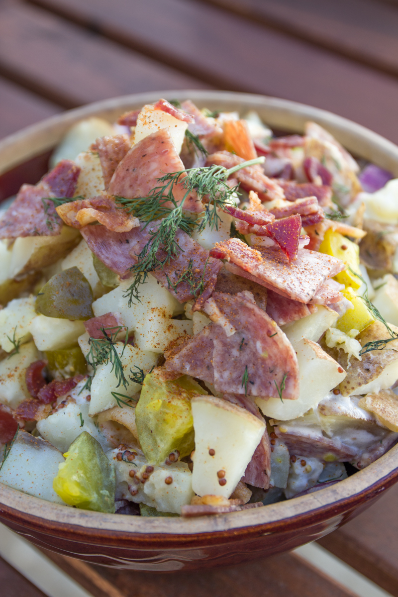 Dill pickles, bacon, and salami. These are essentials for one amazing summer potato salad. You won't need to bring back any leftovers if you make this Meaty Dill Pickle Potato Salad for your next barbecue.