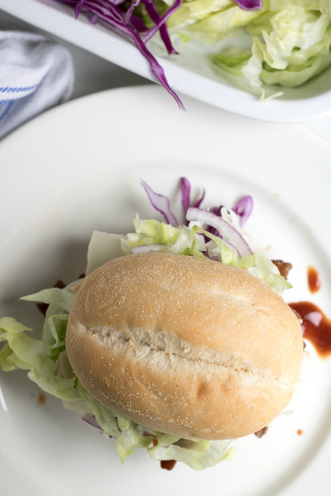 No one will be able to resist these Slow Cooker BBQ Slider Sandwiches! These savory BBQ Sliders are perfect for an easy dinner, potluck, or any gathering served with shaved lettuce, shaved crunchy red cabbage, red onion, and cheese.
