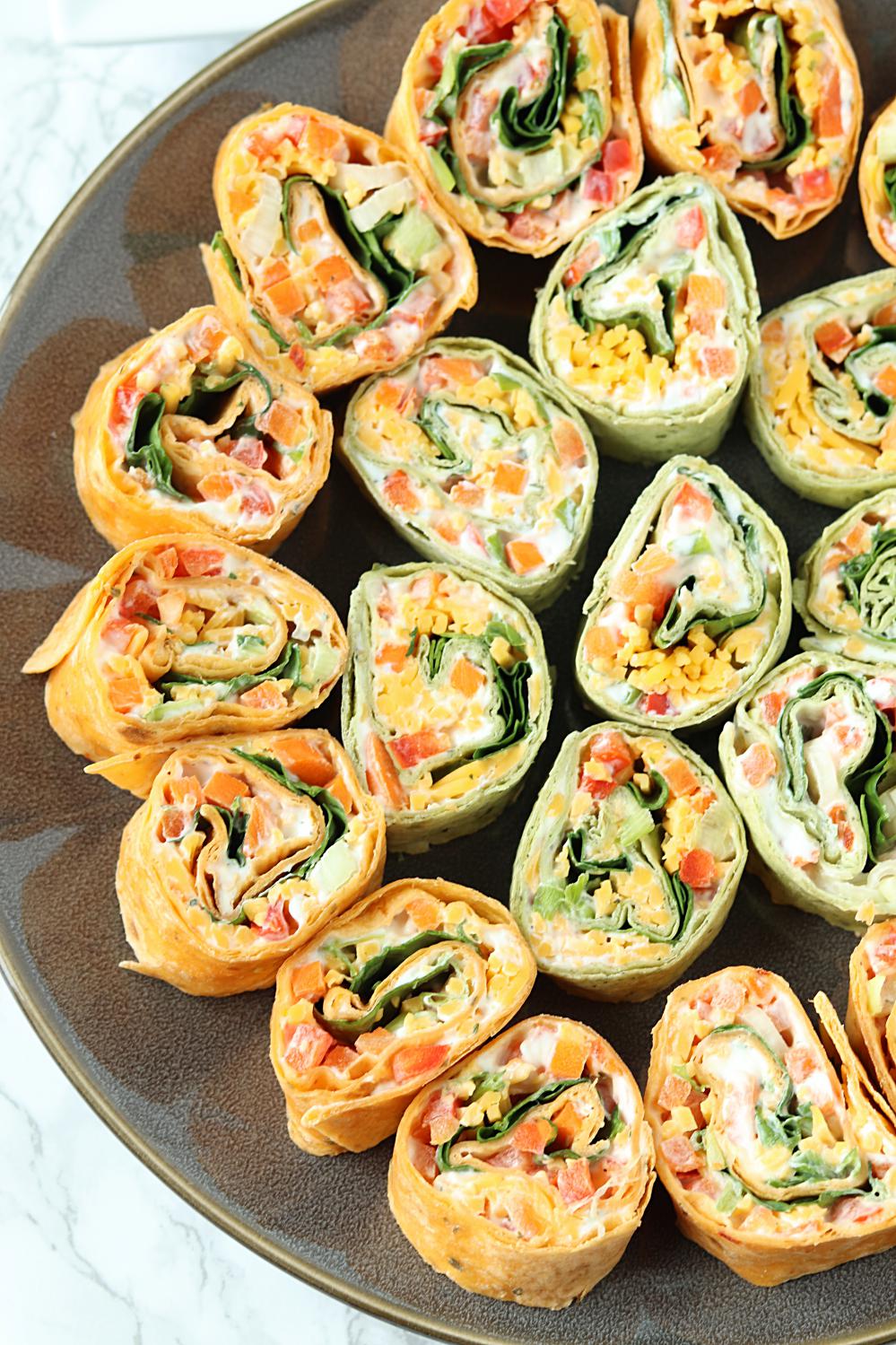 This Veggie Pinwheels Party Appetizer is perfect for tailgating, holiday get togethers, or potlucks. Farmers market veggies, ranch cream cheese spread, and shredded cheese wrapped in tortillas and cut into small bites for snacking!