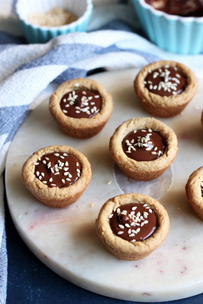 These delightfully indulgent Tahini Cookie Cups are filled with Tahini Chocolate Ganache and finished with a sprinkle of sesame seeds. Ready in just 30 minutes, these cookie cups are what you need when you're craving the perfect bite-sized dessert!