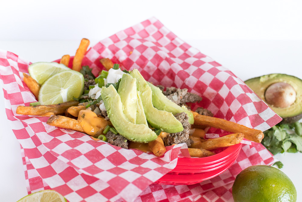Celebrate cheat day with an over-the-top helping of Loaded Cheesy Taco Fries! Seasoned french fries are topped with taco seasoned beef, cheese sauce, sour cream, avocado, and more! Perfect for happy hour entertaining at home.
