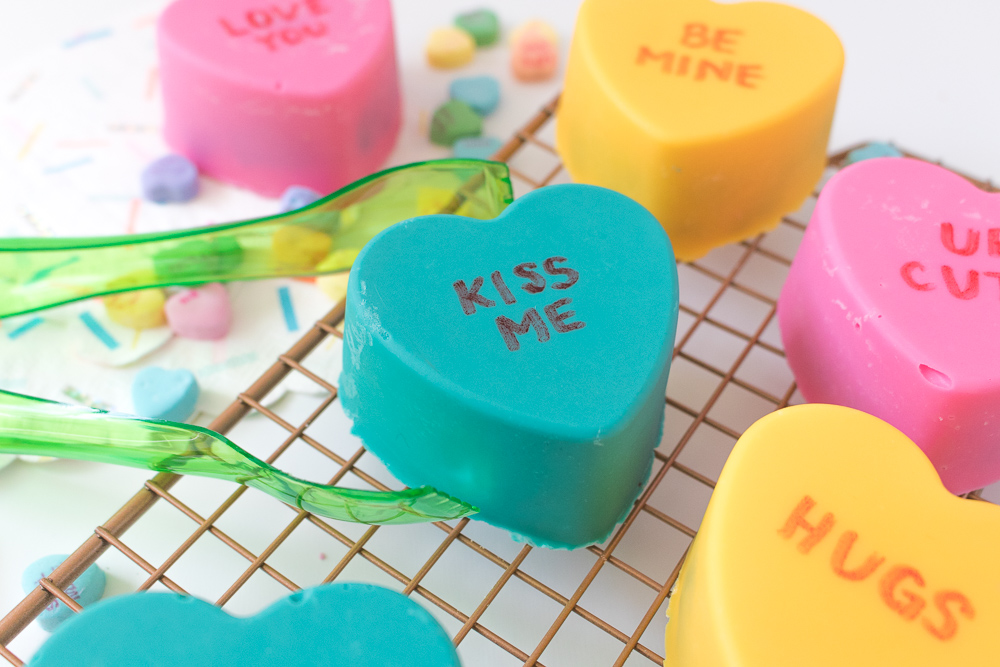 Cute and colorful, these Conversation Heart Cake Bombs are simple to make! Candy-coated chocolate cake with cute little sayings are the perfect way to show loved ones you care this Valentine's Day!