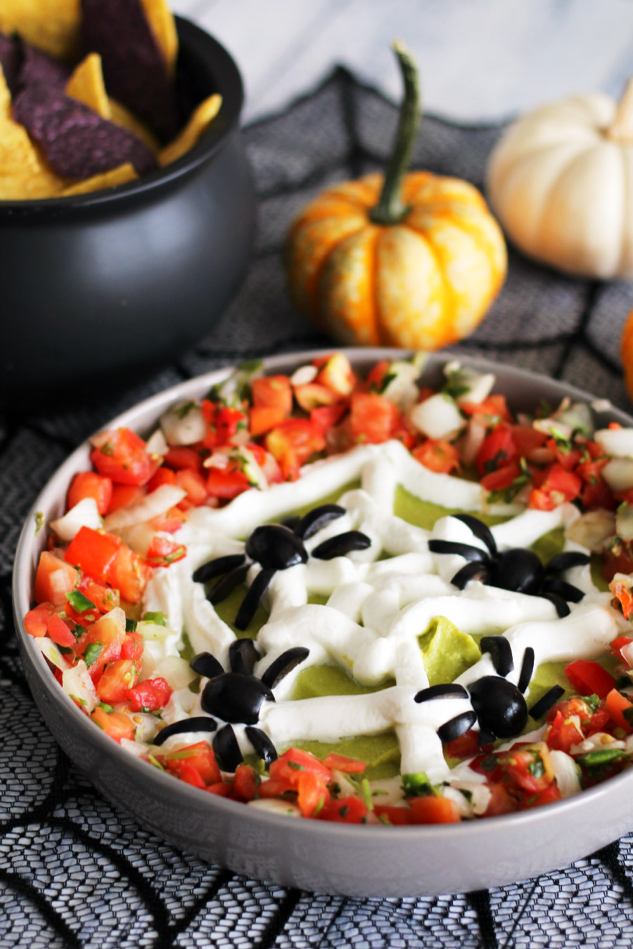 Enjoy spooky snacking with this Halloween Spiderweb Avocado Hummus Dip at your Halloween party! This healthy Halloween recipe is made like traditional hummus, but with avocado, a plain Greek yogurt spiderweb, black olive spiders, and pico de gallo!
