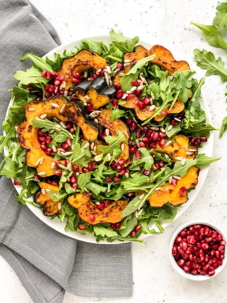 This Roasted Acorn Squash Salad is full of peppery arugula, sunflower seeds, pomegranate seeds, and topped with a simple homemade vinaigrette. A winter salad that's perfect for a weeknight dinner or healthy lunch.