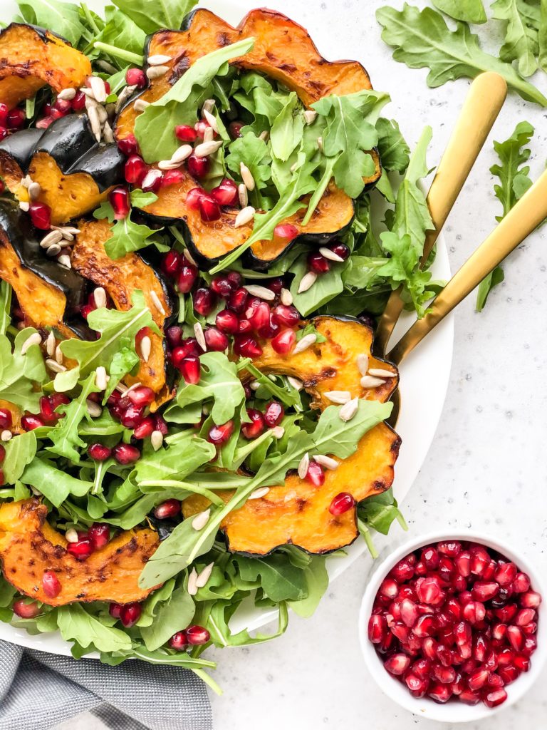 This Roasted Acorn Squash Salad is full of peppery arugula, sunflower seeds, pomegranate seeds, and topped with a simple homemade vinaigrette. A winter salad that's perfect for a weeknight dinner or healthy lunch.